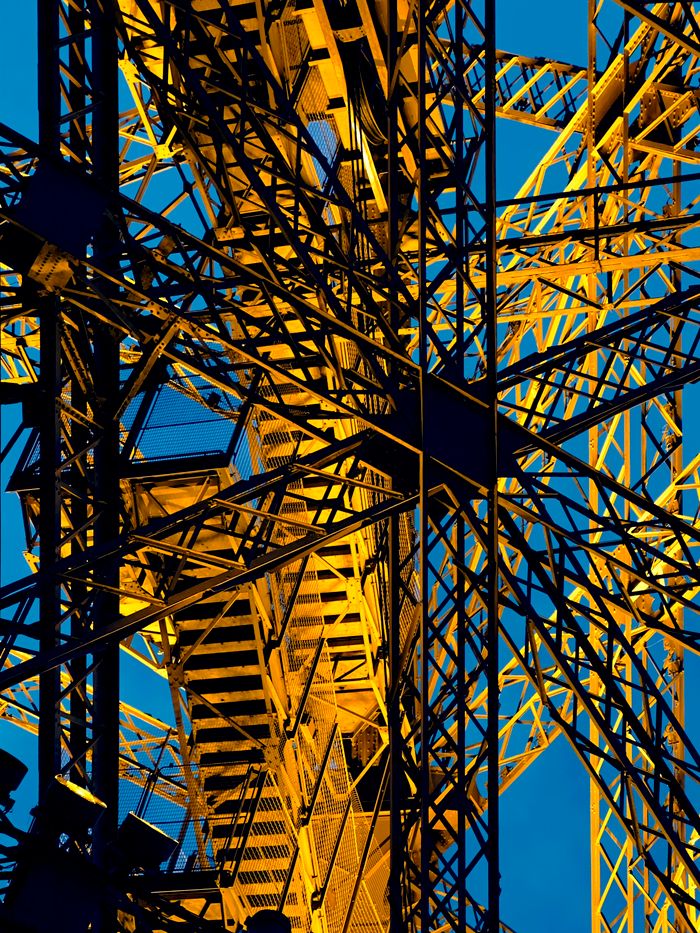 Services Close-up of industrial steel beams illuminated in gold, set against a clear blue sky.